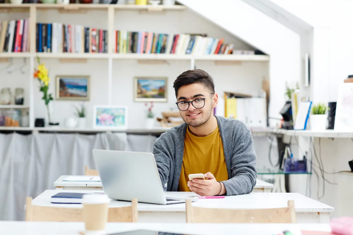 Student smiling at his desk with a laptop and phone