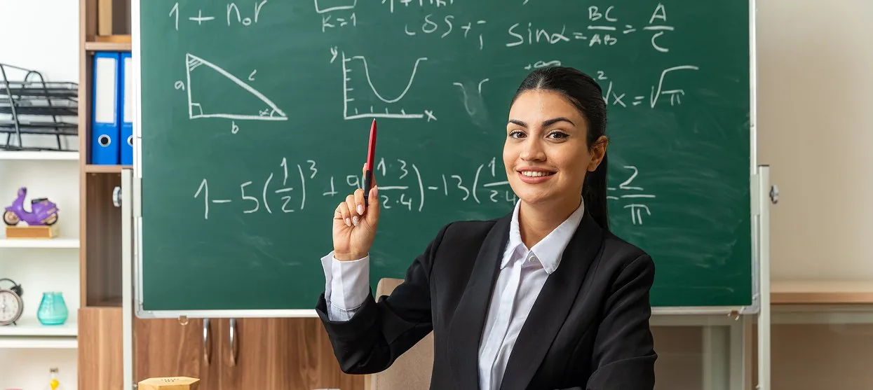 Smiling teacher at a chalkboard covered in maths