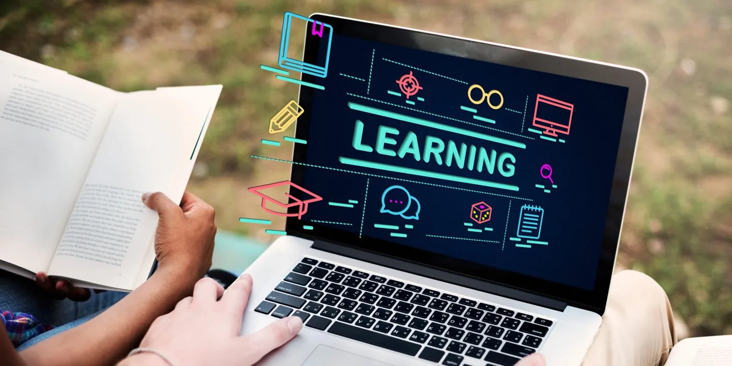 Laptop showing a learning dashboard next to an open book