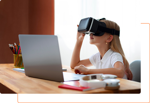 A girl wearing a virtual reality headset sits at a desk in front of a laptop