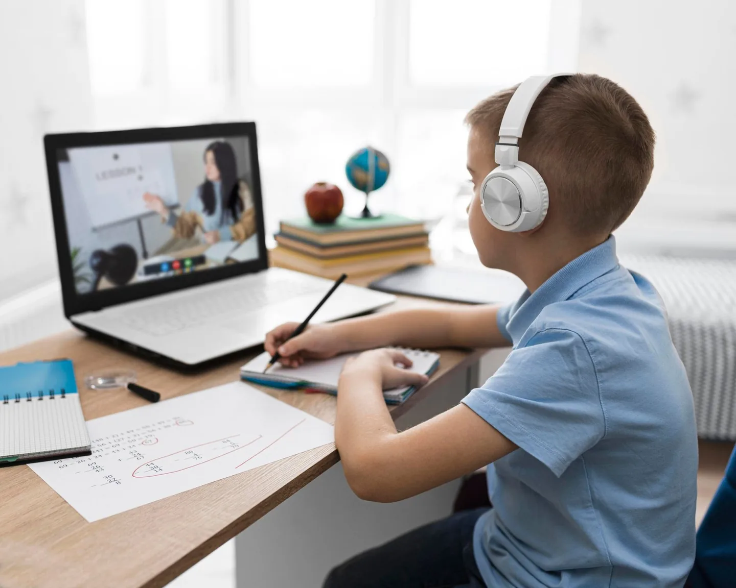 Boy with headphones taking notes during an online class