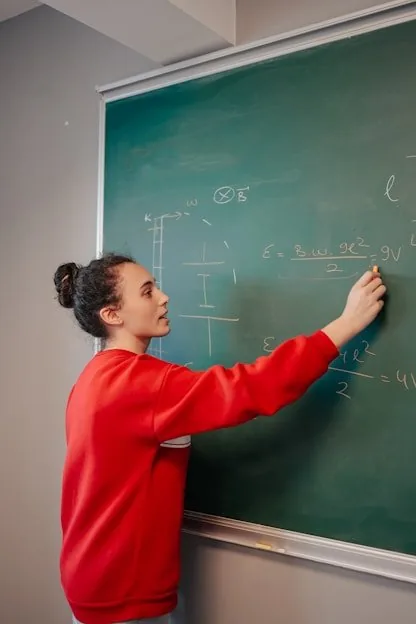 A teacher writing equations on a green chalkboard
